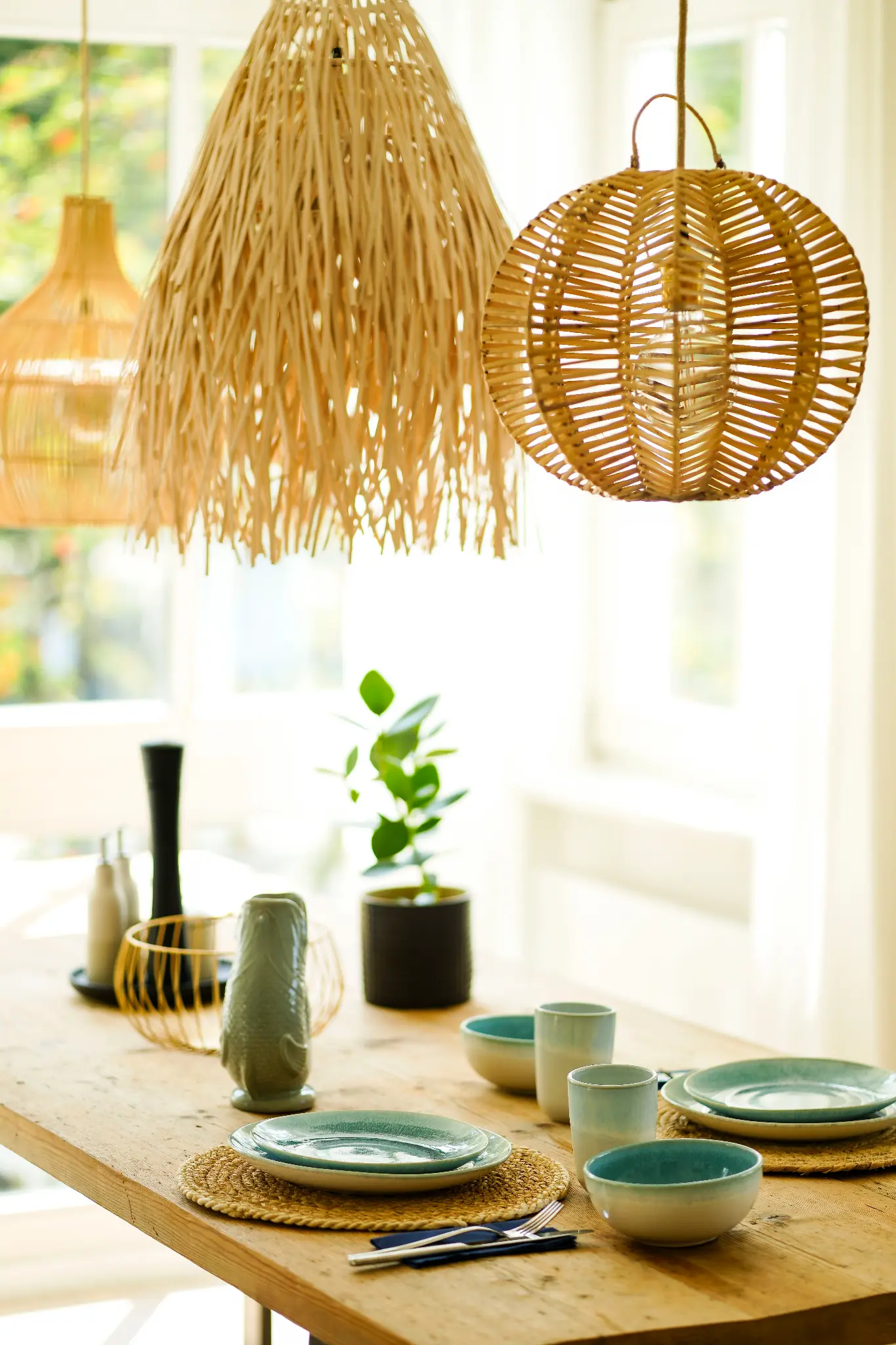 Gedeckter Esstisch aus Holz mit Rattanleuchten am Fenster